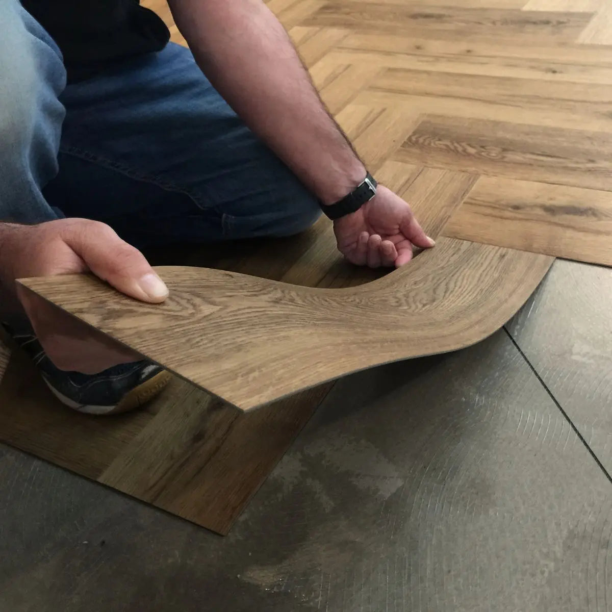 Person installing wood effect LVT flooring in a herringbone pattern on indoor floor in Kingston, Chessington, Surbiton, Epsom, Sutton, Richmond, Wimbledon, Guildford, Croydon, Bromley, Twickenham, Woking, Wembley, Harrow, Feltham, Streatham, Canary Wharf Estate, Greenwich, Brixton, Hanslow, Windsor, Chelsea, Fulham, Lambeth, Westminster, Kensington, Camden Town, Kennington, Southwark, Putney, South West London, central London