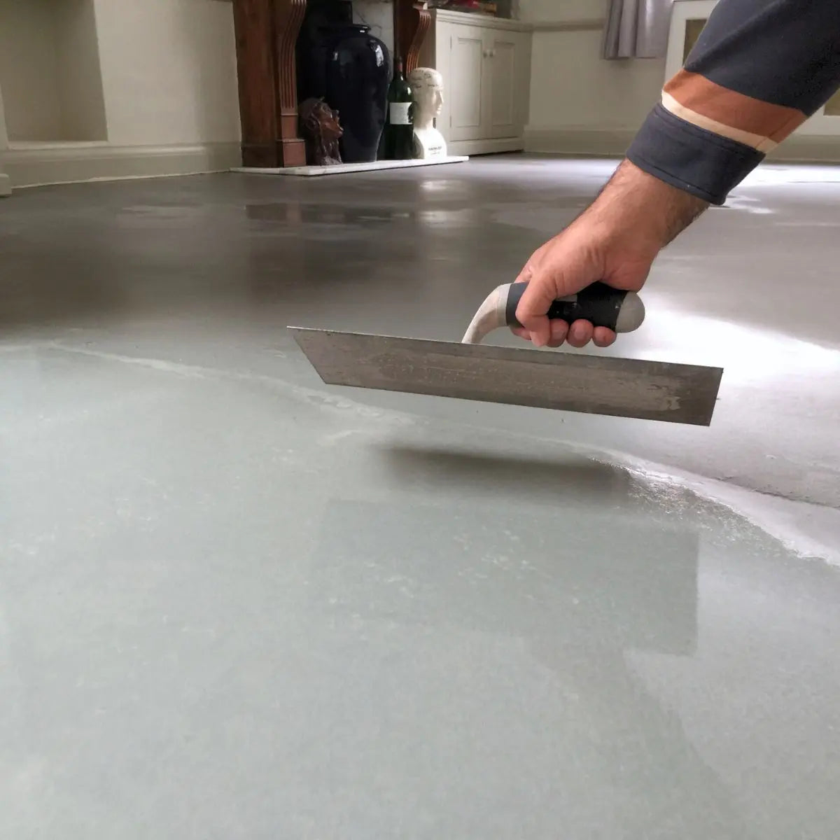 Hand leveling subfloor with trowel during flooring preparation in a modern room