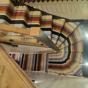 Modern staircase with striped carpet featuring brown, beige, black, and orange tones.