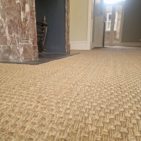 Sisal natural carpet installation in a modern living room with a stone fireplace.